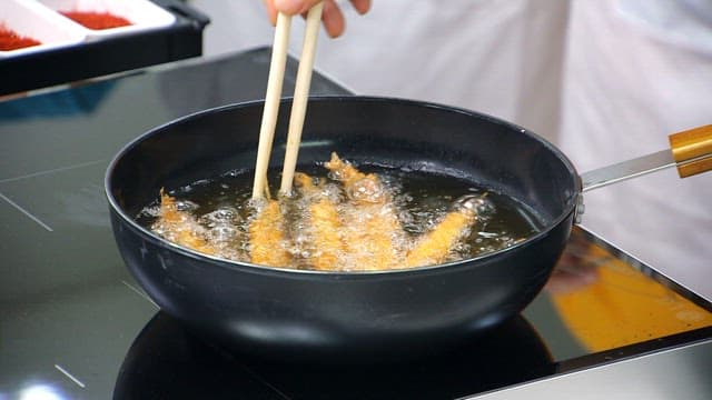 Frying sand eels with skewers in a pan with chopsticks