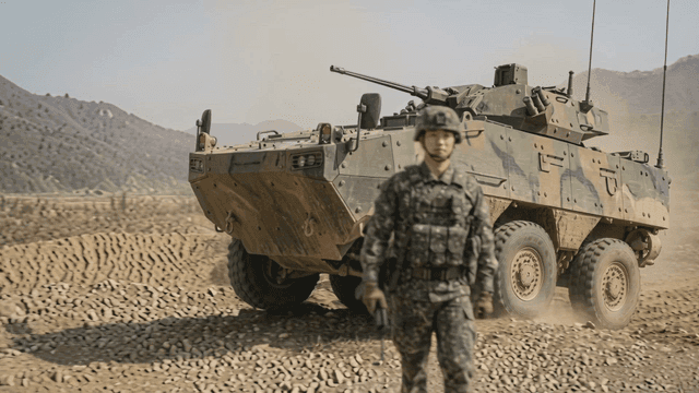 Soldier standing next to armored vehicle in dusty field