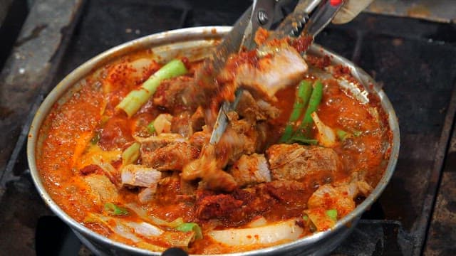 Cutting the meat of the spicy braised ribs boiling on the gas stove