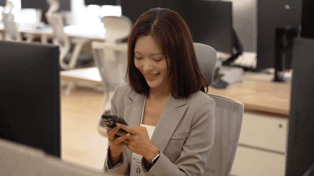 Female office worker smiling while looking at her smartphone in office