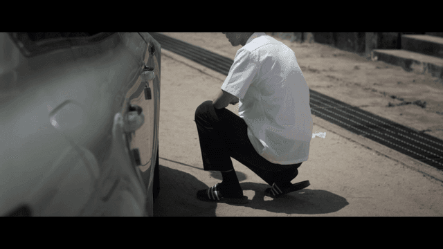 Student crouching with knife in hand beside parked car in distress