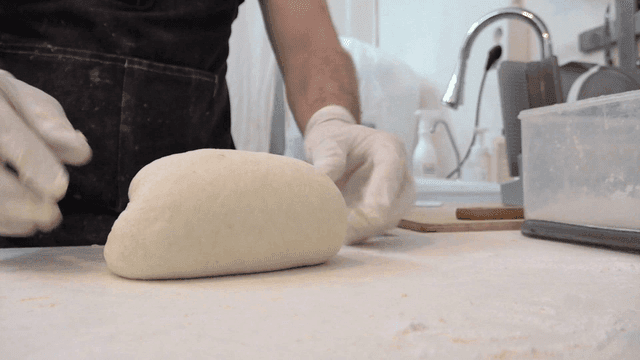 Baker kneading elastic bread dough in kitchen