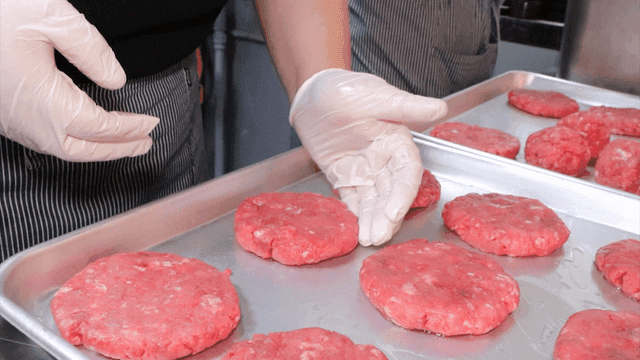 Gloved hands shaping raw meat patties