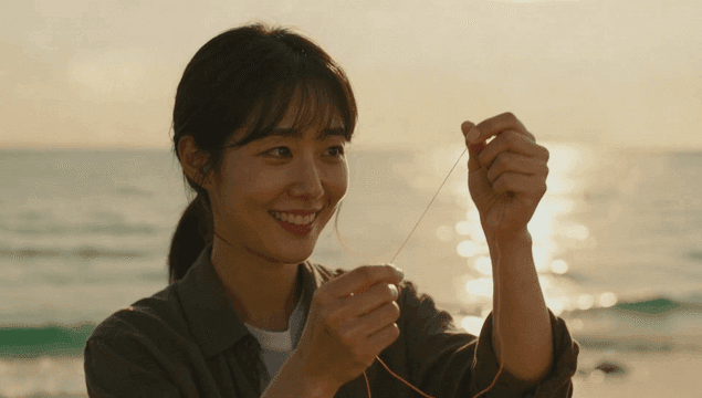Woman smiling while looking at thread on beach at sunset