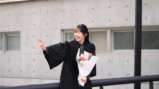 Graduates waving and holding flowers at graduation ceremony