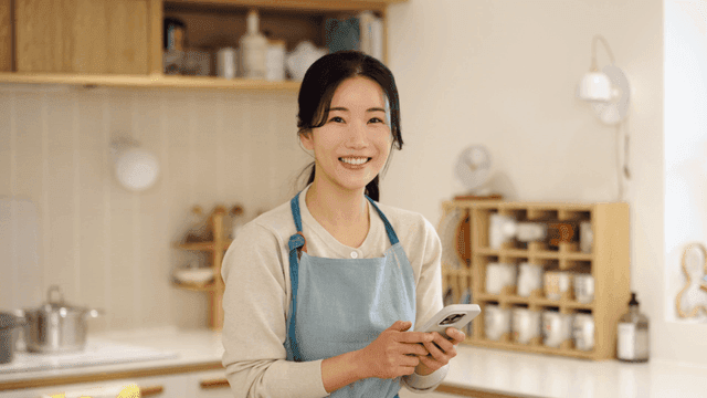 Smiling woman holding cell phone in cozy kitchen