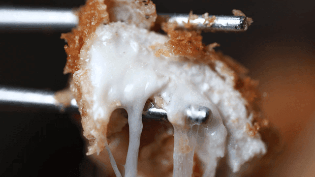 Chopsticks picking up pork cutlet with melted cheese