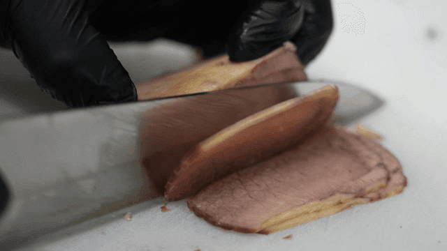 Beef brisket being sliced ​​with knife on cutting board