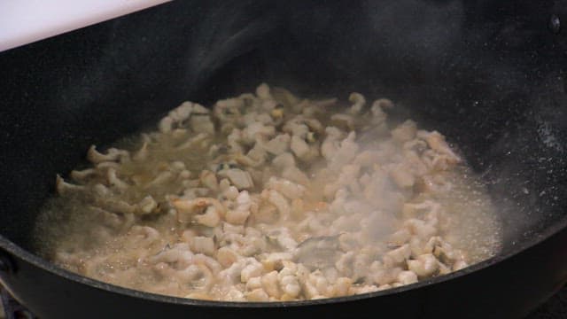 Cooking seafood in a frying pan with trimmed eel and green onions