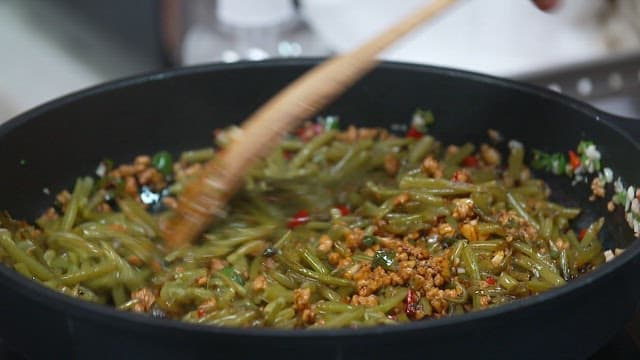 Stir-frying sweet potato stem in a hot skillet with a wooden spatula.