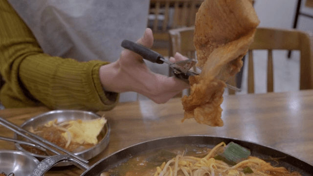 A person cutting meat for a hot stew with scissors