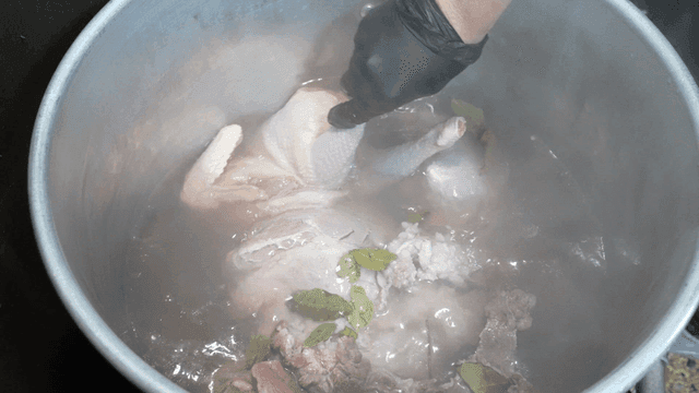Chicken being boiled with herbs in a pot
