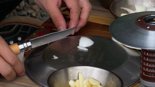 Chopping onion and carrot with a small knife on a metal plate on a wooden table