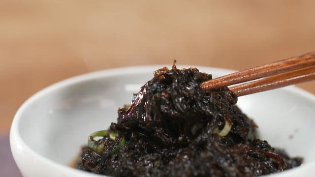 Picking up warm seaweed dish in a bowl with chopsticks