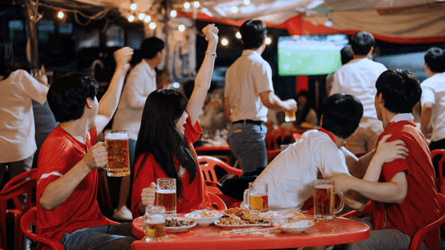 Friends cheering while watching soccer match at street food stall