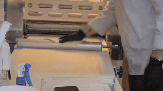 작업대에서 밀대로 반죽을 말아 붙이는 제빵사