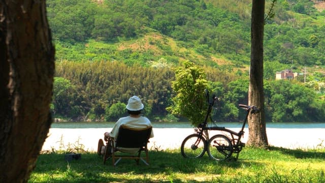 Person relaxing on a chair by the riverside with a bicycle