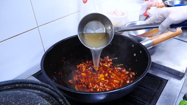 The process of pouring water into red pepper oil and adding various seafood