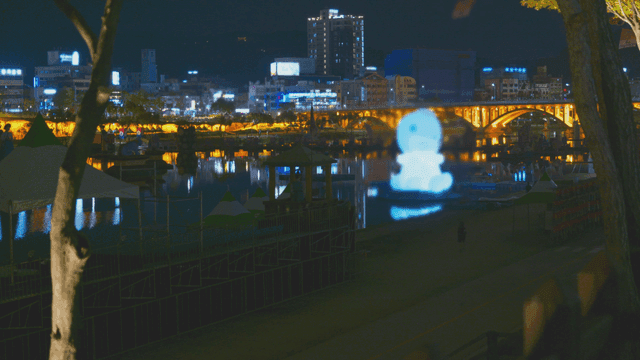 Night scene with bridge and city lights above floating sculpture
