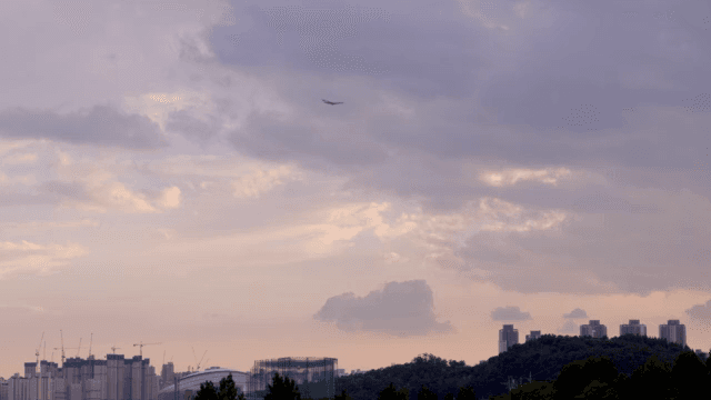 구름 낀 저녁 하늘을 지나가는 비행기와 도시 스카이라인