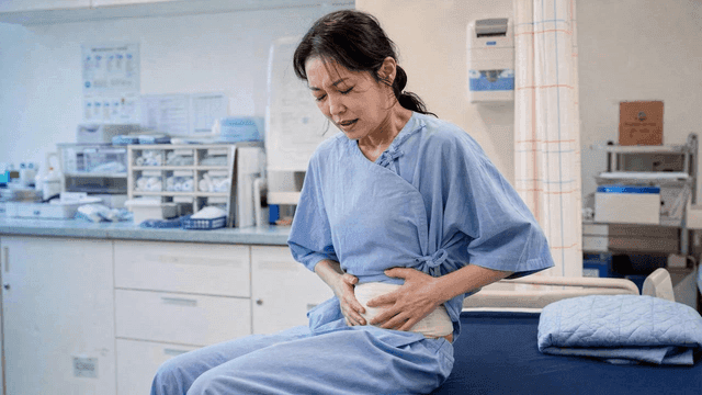 Woman wearing hospital gown and holding her abdomen