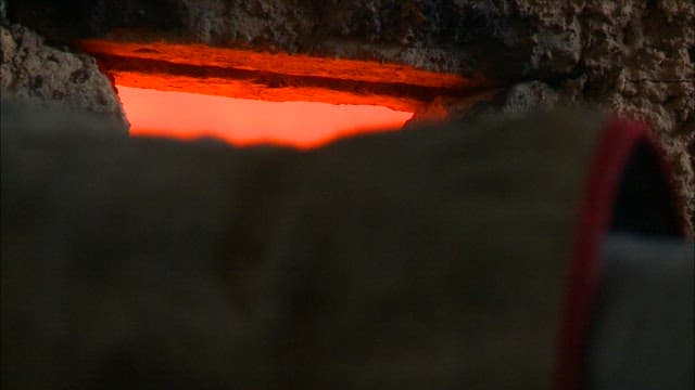 Firewood being placed in a hot forge with flames rising