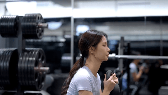 케틀벨로 스쿼트 운동하는 젊은 여성의 옆모습