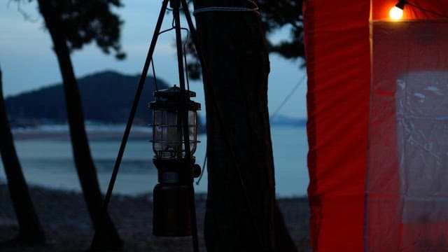 Camping Lantern Being Lit Near a Tent at Dusk