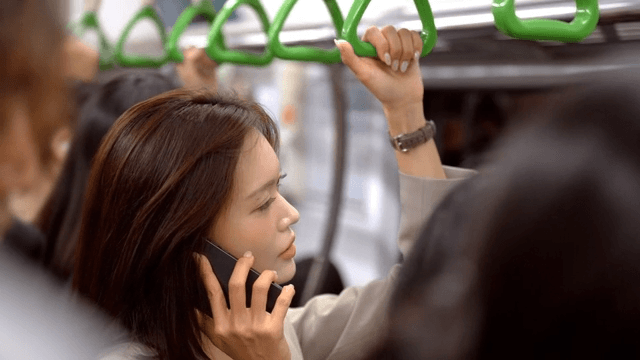 Woman holding onto handrail and talking on her cell phone in crowded subway