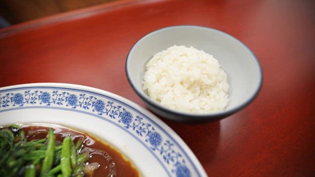 Plate of stir-fried water parsley and a bowl of rice on a wooden table
