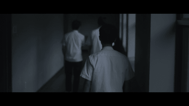 Male student walking again in dark hallway after looking back