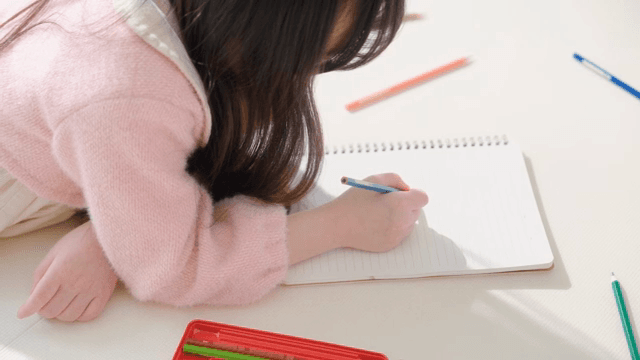 Child writing in a notebook indoors