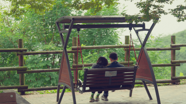 숲 속 공원에서 그네에 앉아 있는 커플