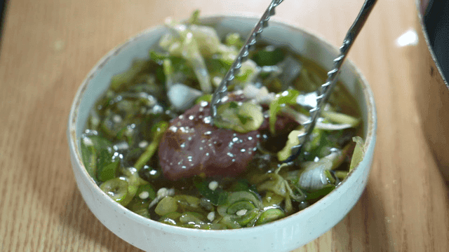 Tongs dipping grilled beef into scallion seasoning sauce
