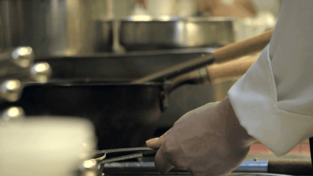 Chef stirring a pot in a busy kitchen