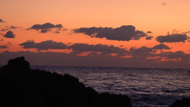 Sunset over the sea with fishing boat passing by with its lights on