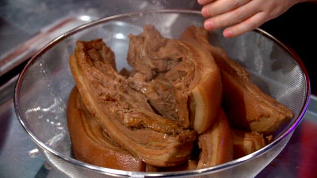 Boiled pork slices being rinsed in a colander