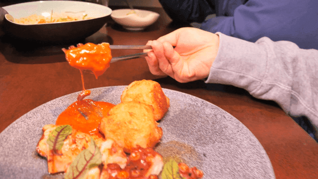 Chopsticks holding grilled octopus with sauce and garnish