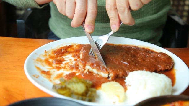 Cutting a breaded pork cutlet with sauce