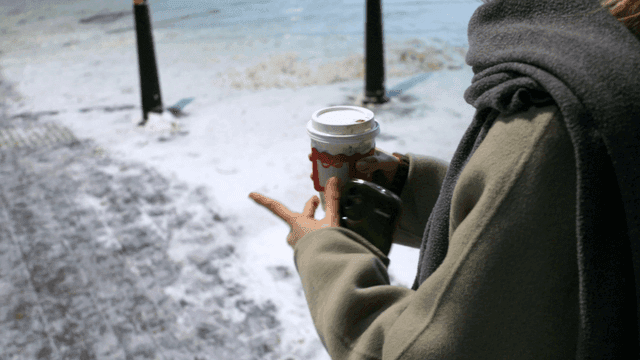 Woman walking along snowy road holding hot drink