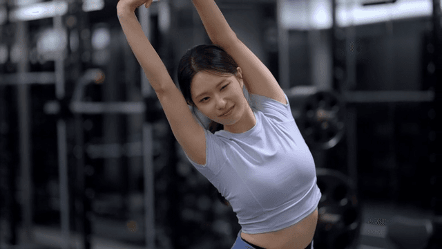 Side view of young woman stretching arms at gym