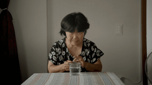 An elderly woman struggling to open a medicine pouch