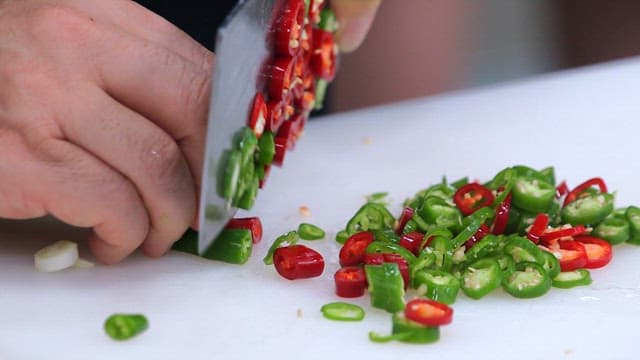 Hands chopping green and red peppers on a white cutting board