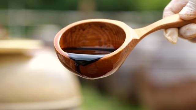 Pouring thick black soy sauce from a wooden ladle outdoors