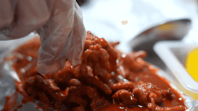 Hands holding spicy chicken feet while wearing gloves