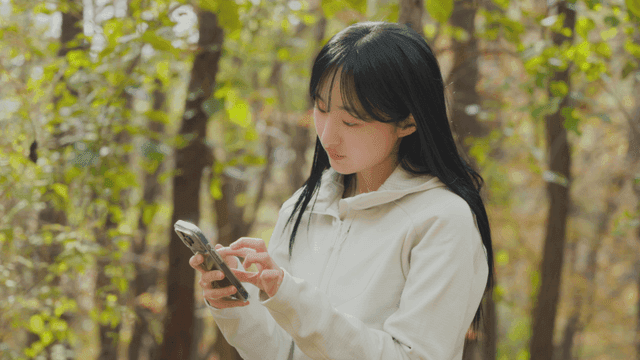 가을 숲에서 스마트폰을 사용하는 여성