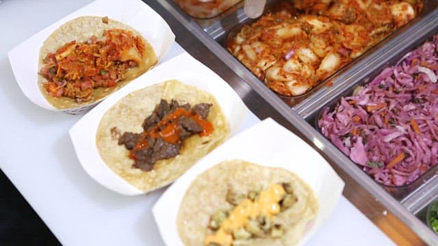 음식 조리대에서 김치와 다양한 재료로 타코를 준비하는 모습