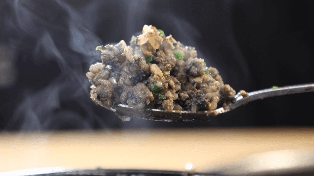 Spoon scooping out steaming hot stone pot rice