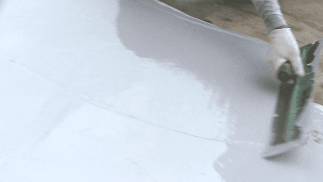 시멘트 바닥에 흰색 페인트 코팅을 바르는 작업자