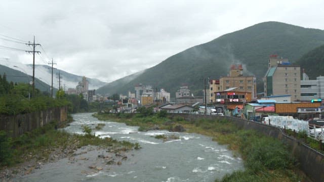 연기가 피어오르는 녹색 산 사이에 자리잡은 작은 마을